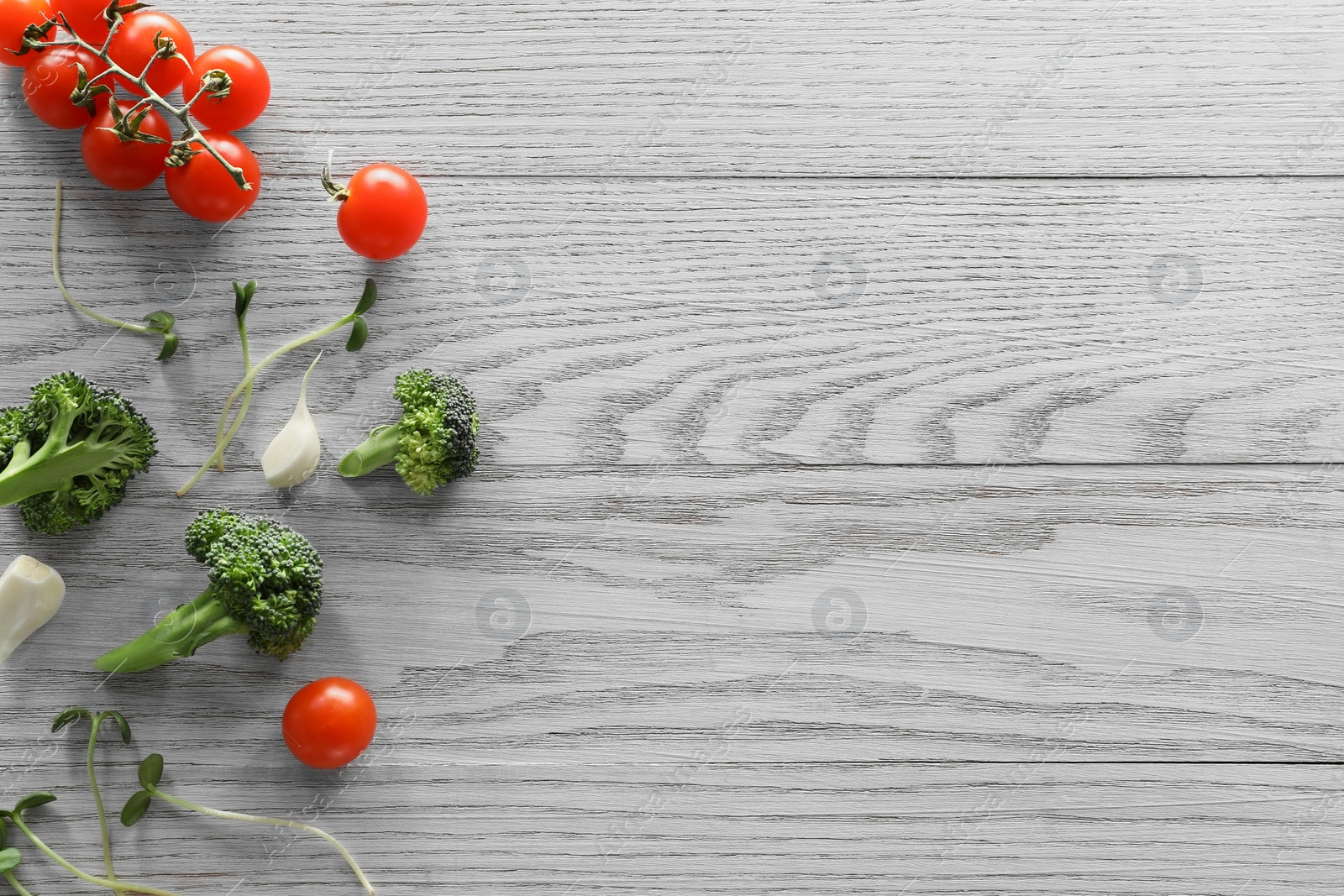 Photo of Food photography. Fresh cherry tomatoes, broccoli, garlic and microgreen on wooden table, flat lay with space for text