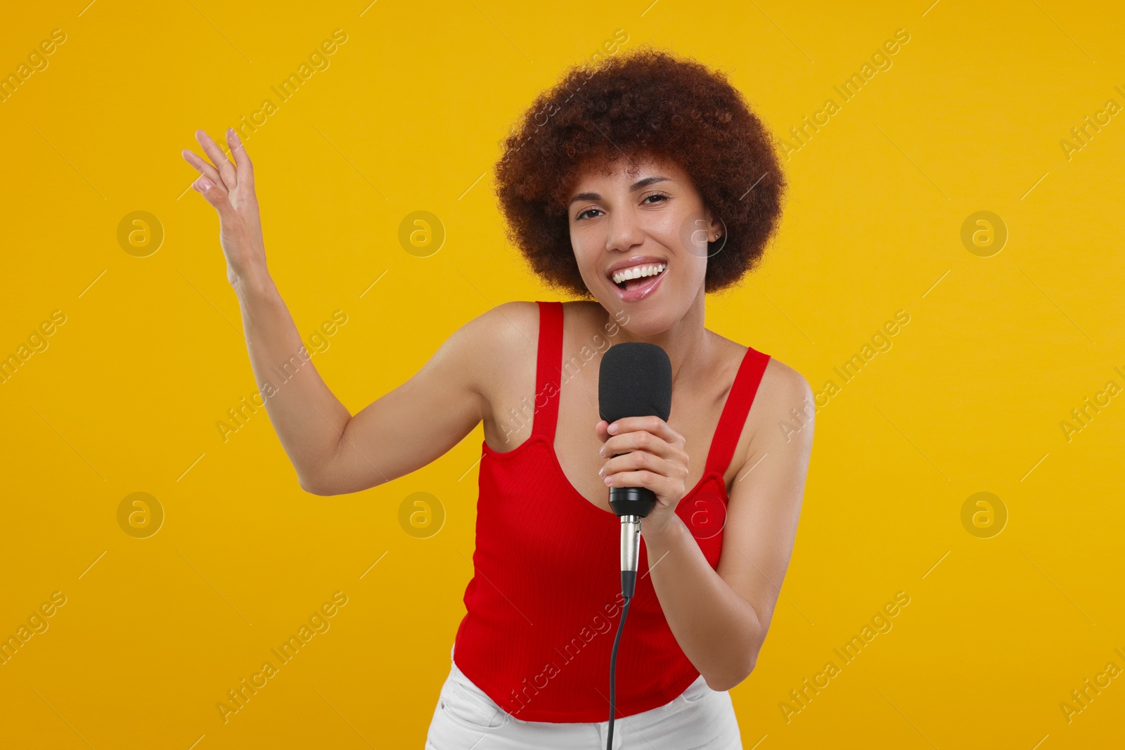 Photo of Curly young woman with microphone singing on yellow background