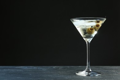 Martini cocktail with ice and olives on grey table against dark background. Space for text