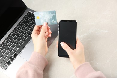 Photo of Online payment. Woman using credit card and smartphone near laptop at light grey table, top view