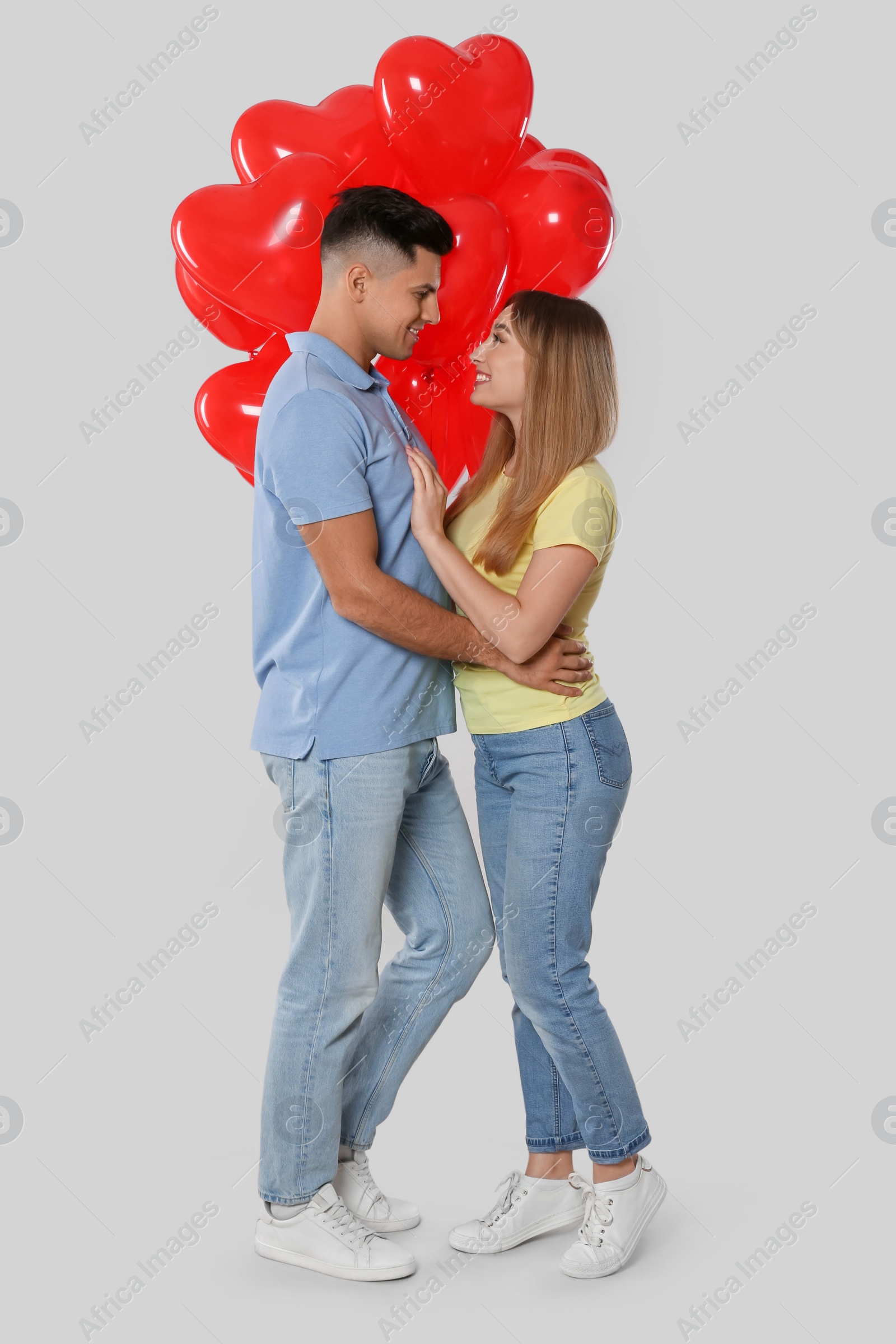 Photo of Lovely couple with heart shaped balloons on light grey background. Valentine's day celebration