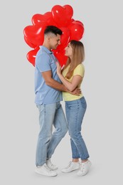 Photo of Lovely couple with heart shaped balloons on light grey background. Valentine's day celebration