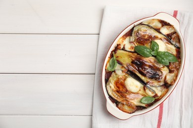 Delicious eggplant lasagna in baking dish and napkin on white wooden table, top view. Space for text