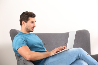 Handsome young man working with laptop on sofa indoors