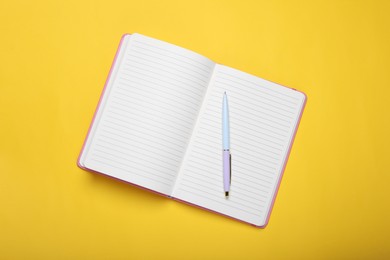 Photo of Open office notebook and pen on yellow background, top view