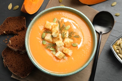 Photo of Delicious pumpkin soup in bowl served on black table, flat lay