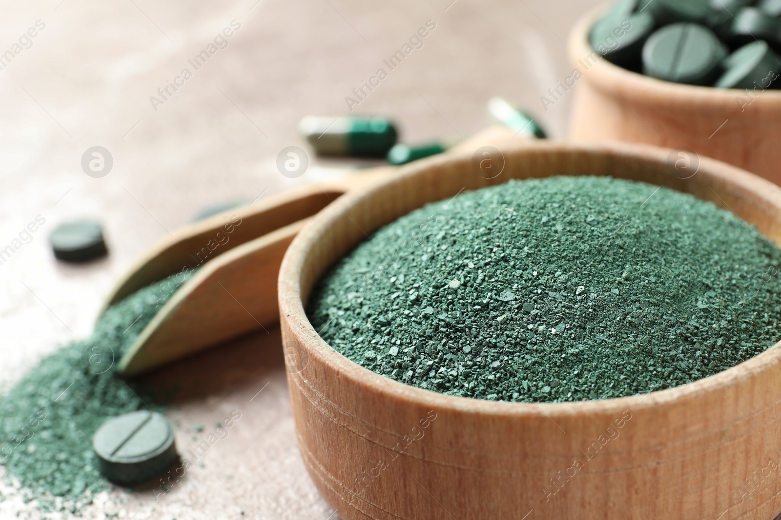 Photo of Spirulina powder in wooden bowl and pills on table, closeup