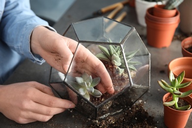 Woman transplanting home plants into florarium at table, closeup