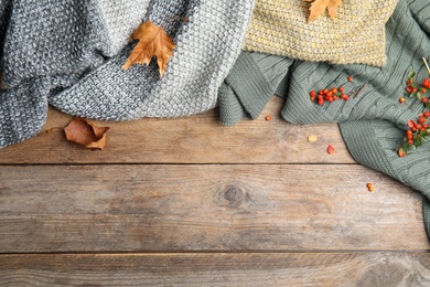 Different plaids with red berries and dry leaves on wooden table, flat lay. Space for text