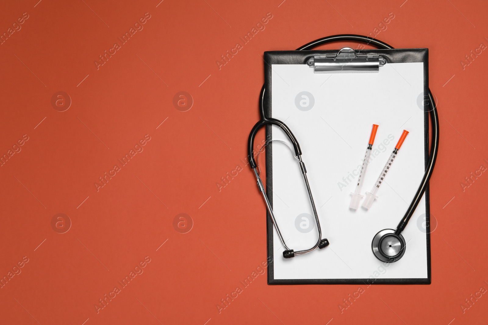 Photo of Stethoscope, syringes and clipboard on crimson background, top view. Space for text