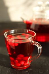 Photo of Tasty hot cranberry tea with fresh berries in glass cup on black textured table