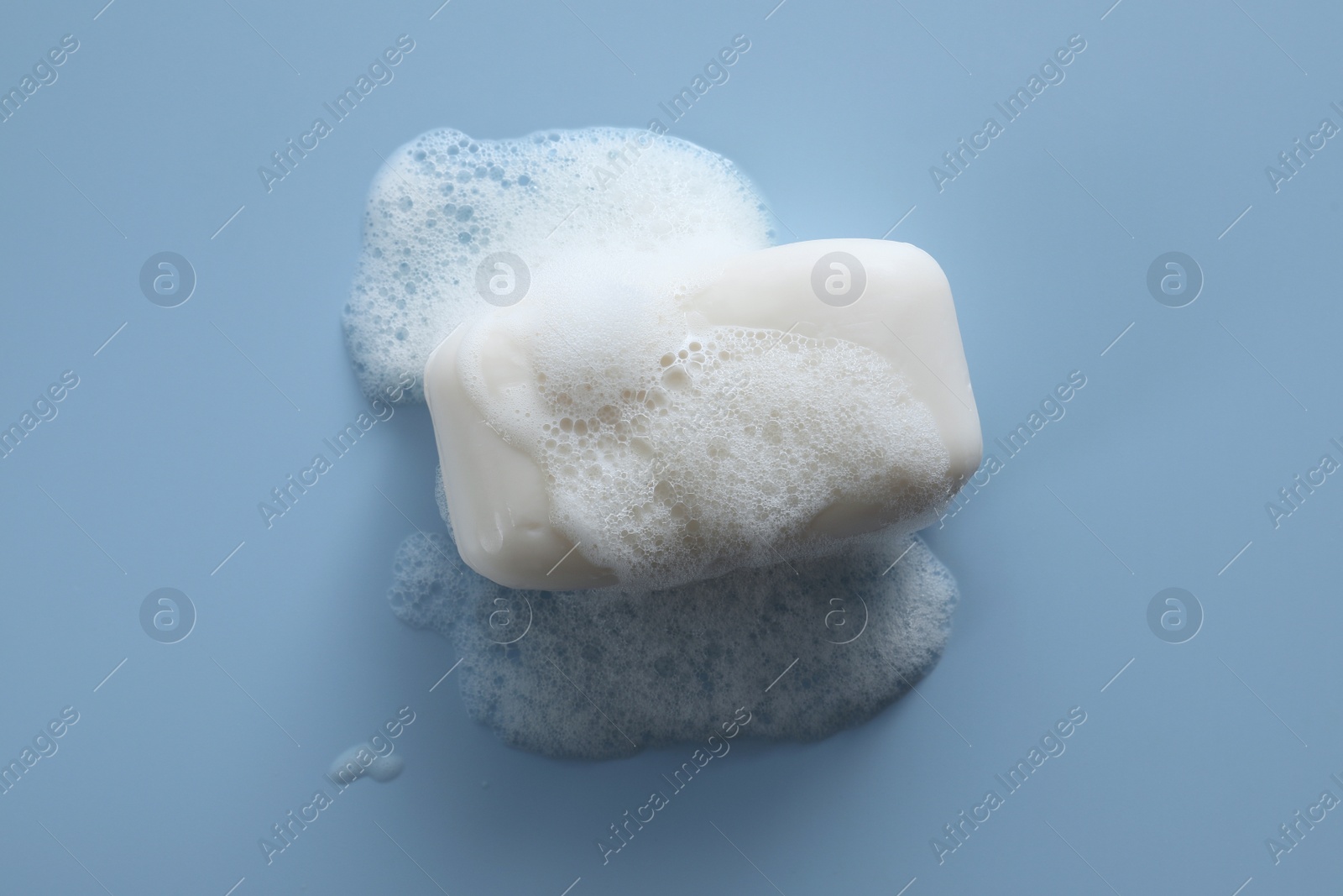 Photo of Soap bar with fluffy foam on light blue background, top view