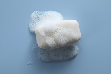 Photo of Soap bar with fluffy foam on light blue background, top view