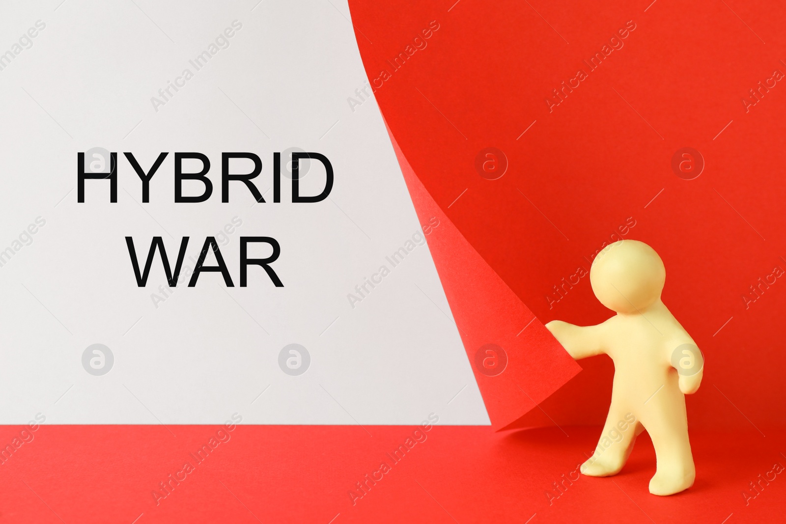 Photo of Human figure made of plasticine showing words Hybrid War on white background hidden behind red paper