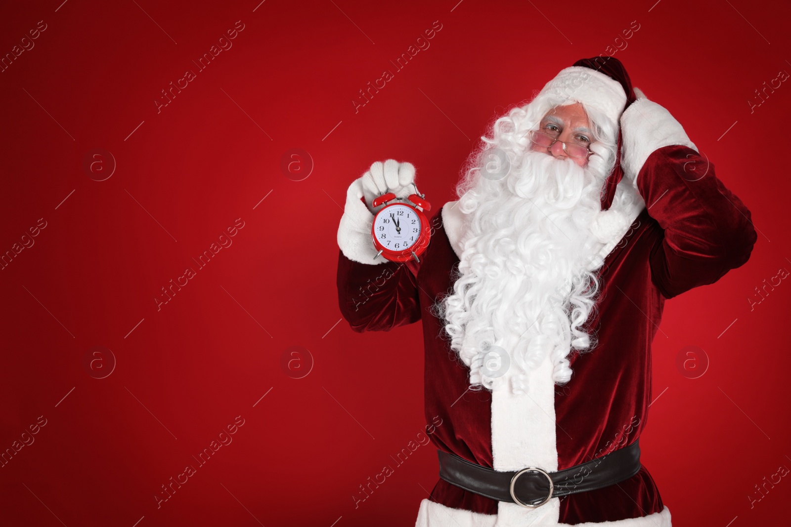 Photo of Santa Claus holding alarm clock on red background, space for text. Christmas countdown