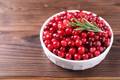 Photo of Fresh ripe cranberries and rosemary in bowl on wooden table, closeup