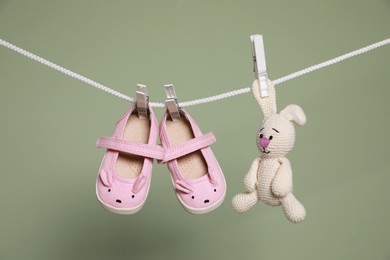 Photo of Cute small baby shoes and toy hanging on washing line against green background