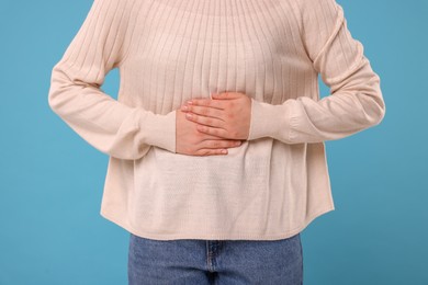 Photo of Woman suffering from abdominal pain on light blue background, closeup. Unhealthy stomach