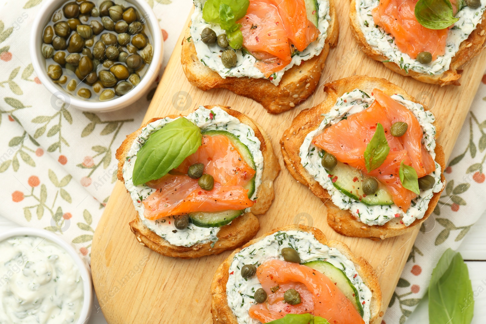 Photo of Tasty canapes with salmon, capers, cucumber and sauce on table, top view