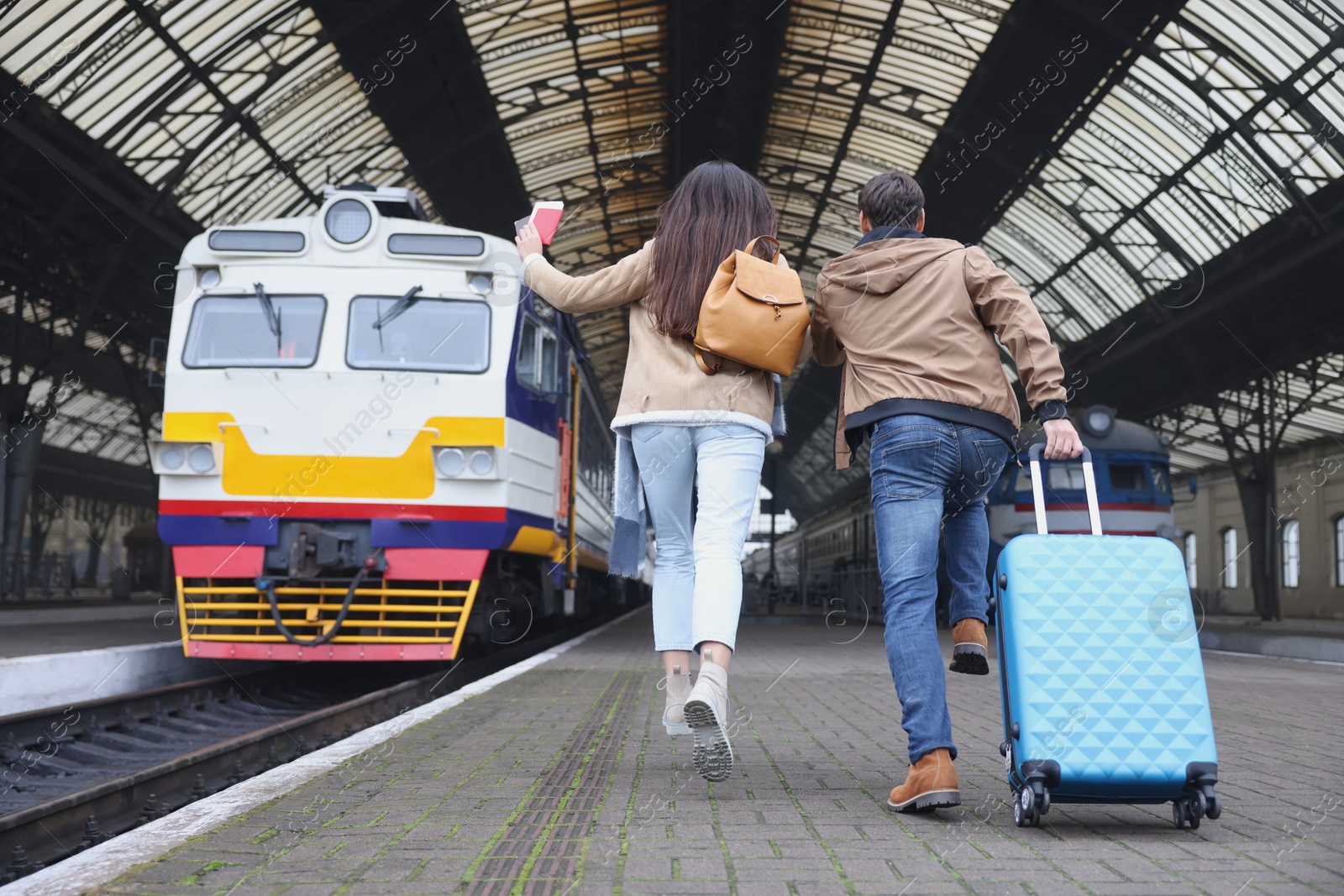 Photo of Being late. Couple with suitcase running towards train at station, back view. Space for text