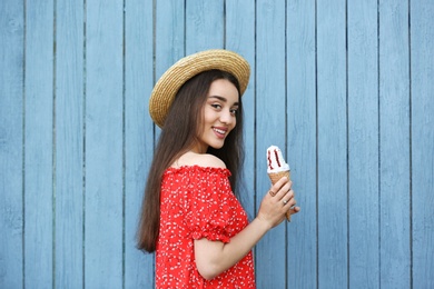 Happy young woman with delicious ice cream in waffle cone near wooden wall