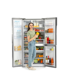 Photo of Young woman with bell pepper near open refrigerator on white background