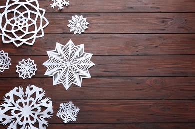 Photo of Flat lay composition with paper snowflakes on wooden background, space for text. Winter season