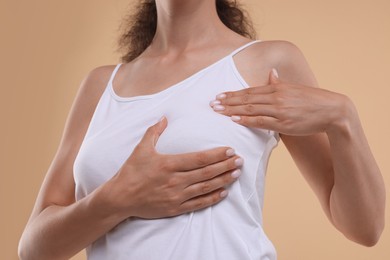 Woman doing breast self-examination on light brown background, closeup