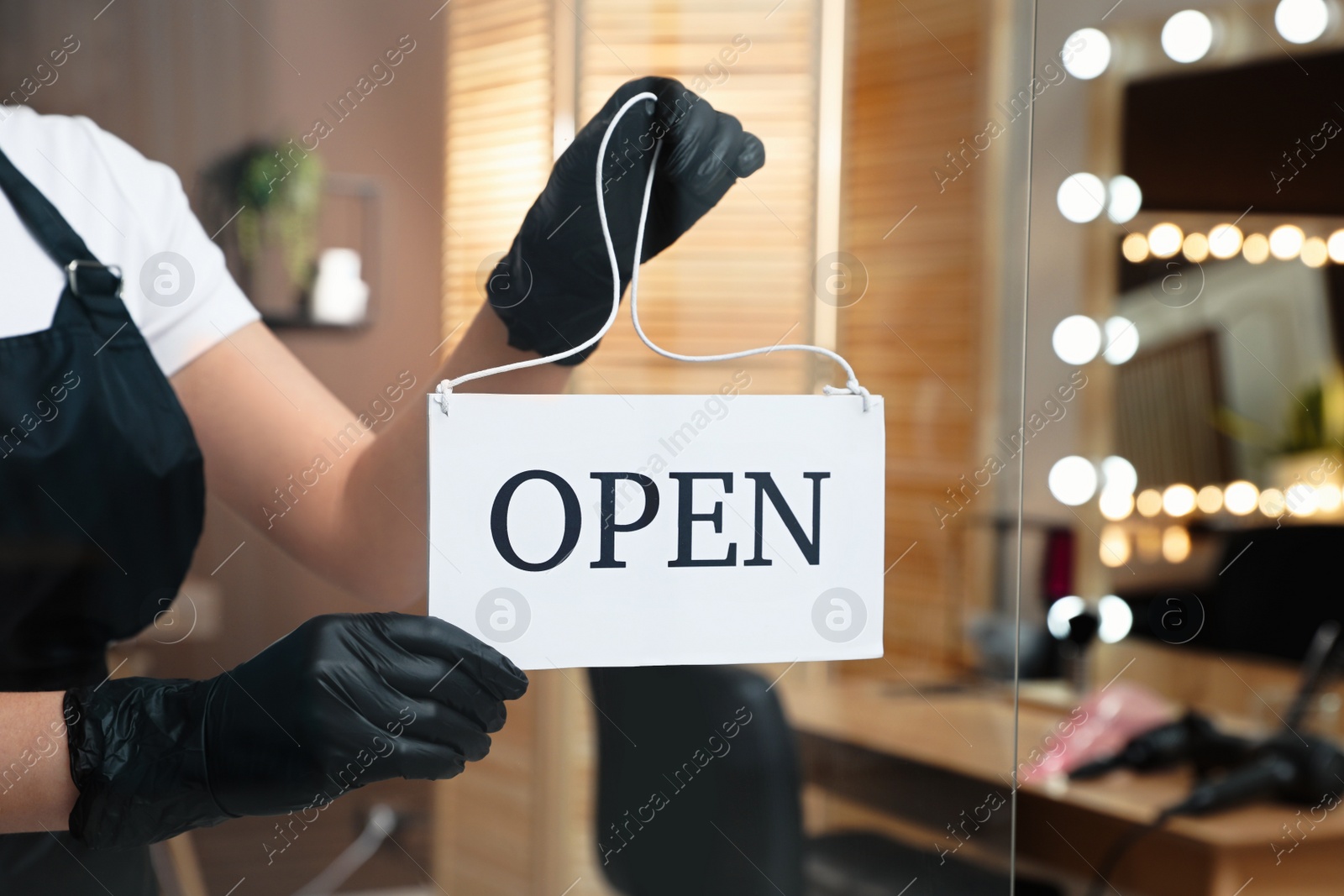 Photo of Woman hanging Open sign onto glass door in salon, closeup. Beauty services during Coronavirus quarantine