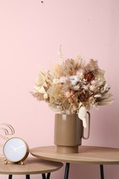 Stylish ceramic vase with dry flowers and leaves on wooden table near pink wall