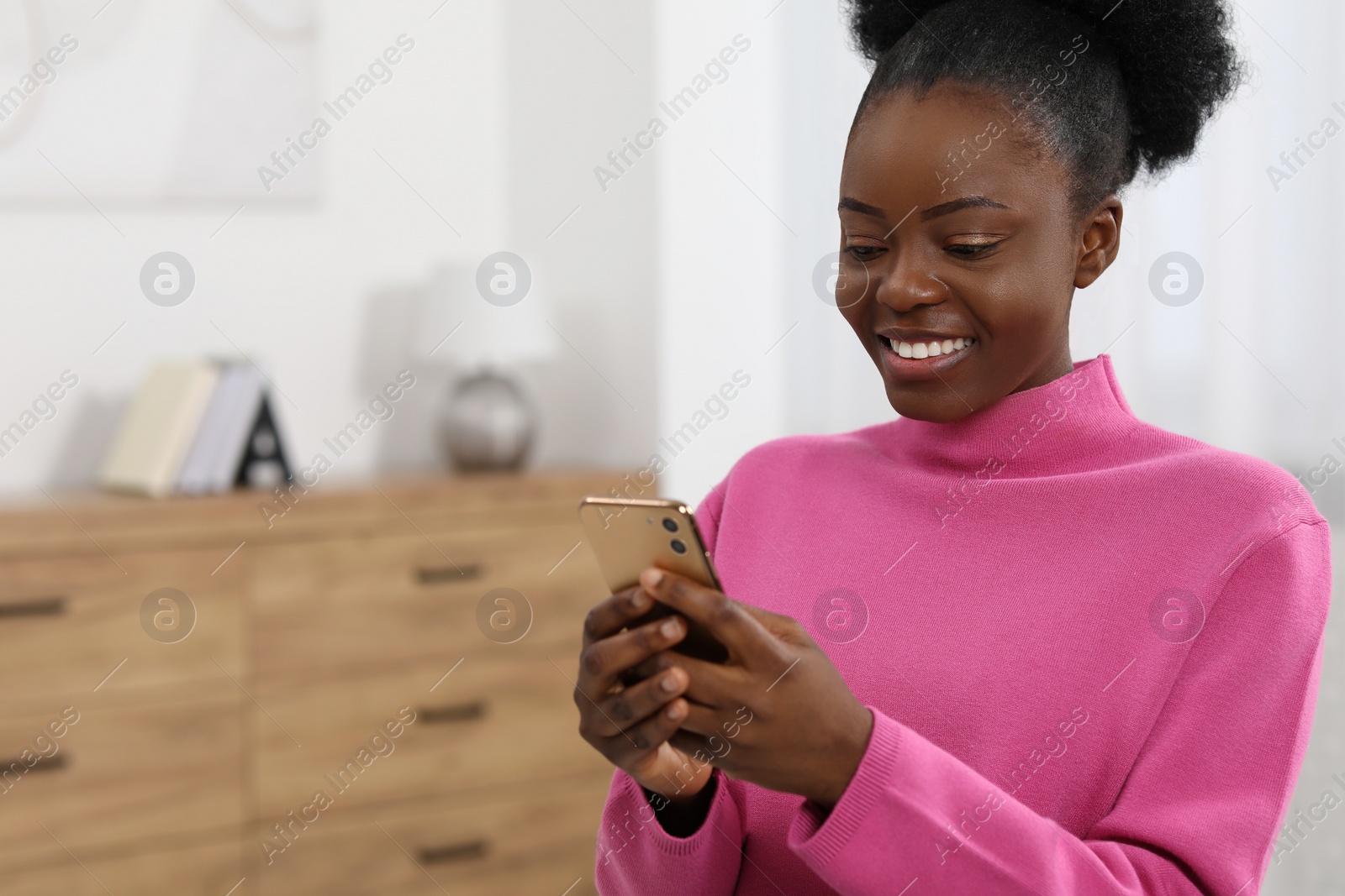 Photo of Happy young woman using smartphone at home. Space for text
