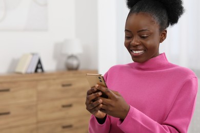 Happy young woman using smartphone at home. Space for text