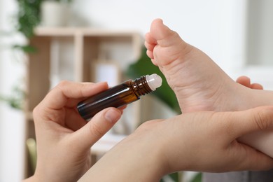 Mother applying essential oil from roller bottle onto her baby`s heel indoors, closeup