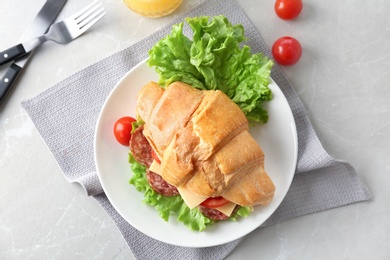 Photo of Tasty croissant sandwich with salami on table, top view