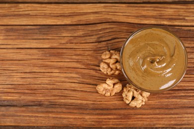 Photo of Delicious nut butter in bowl and walnuts on wooden table, top view. Space for text