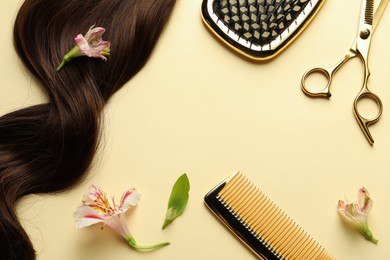 Hairdresser tools. Brown hair lock, comb, scissors and flowers on pale yellow background, flat lay. Space for text