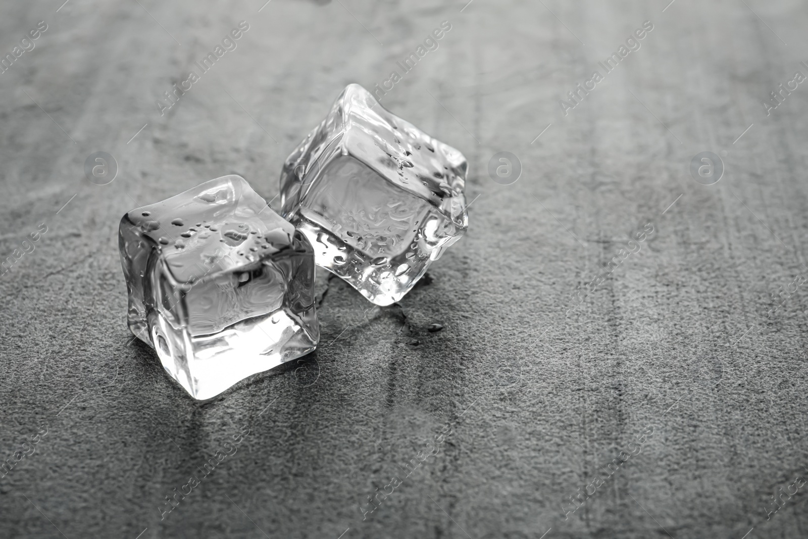 Photo of Crystal clear ice cubes with water drops on metal surface. Space for text