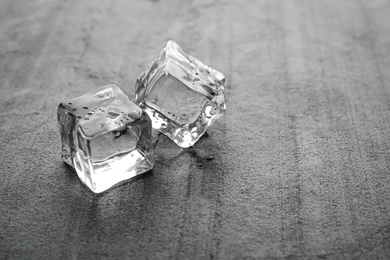 Photo of Crystal clear ice cubes with water drops on metal surface. Space for text