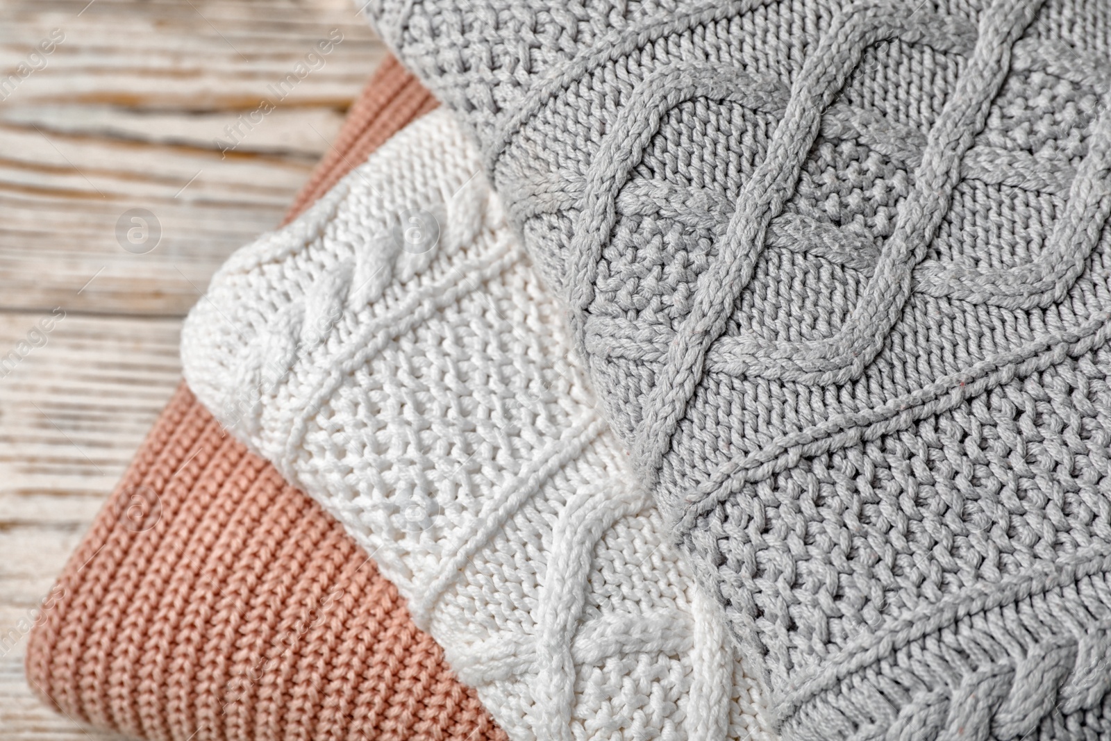 Photo of Stack of folded knitted sweaters on table, closeup