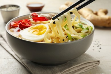 Photo of Eating delicious ramen with chopsticks at light table, closeup. Noodle soup