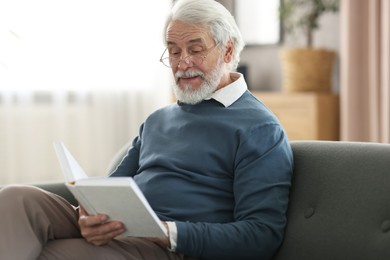 Photo of Portrait of happy grandpa reading book on sofa indoors