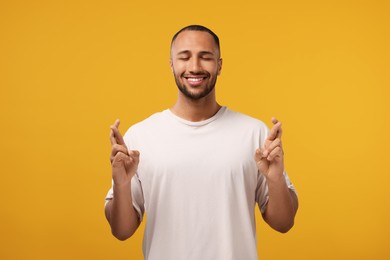 Photo of Happy man crossing his fingers on orange background
