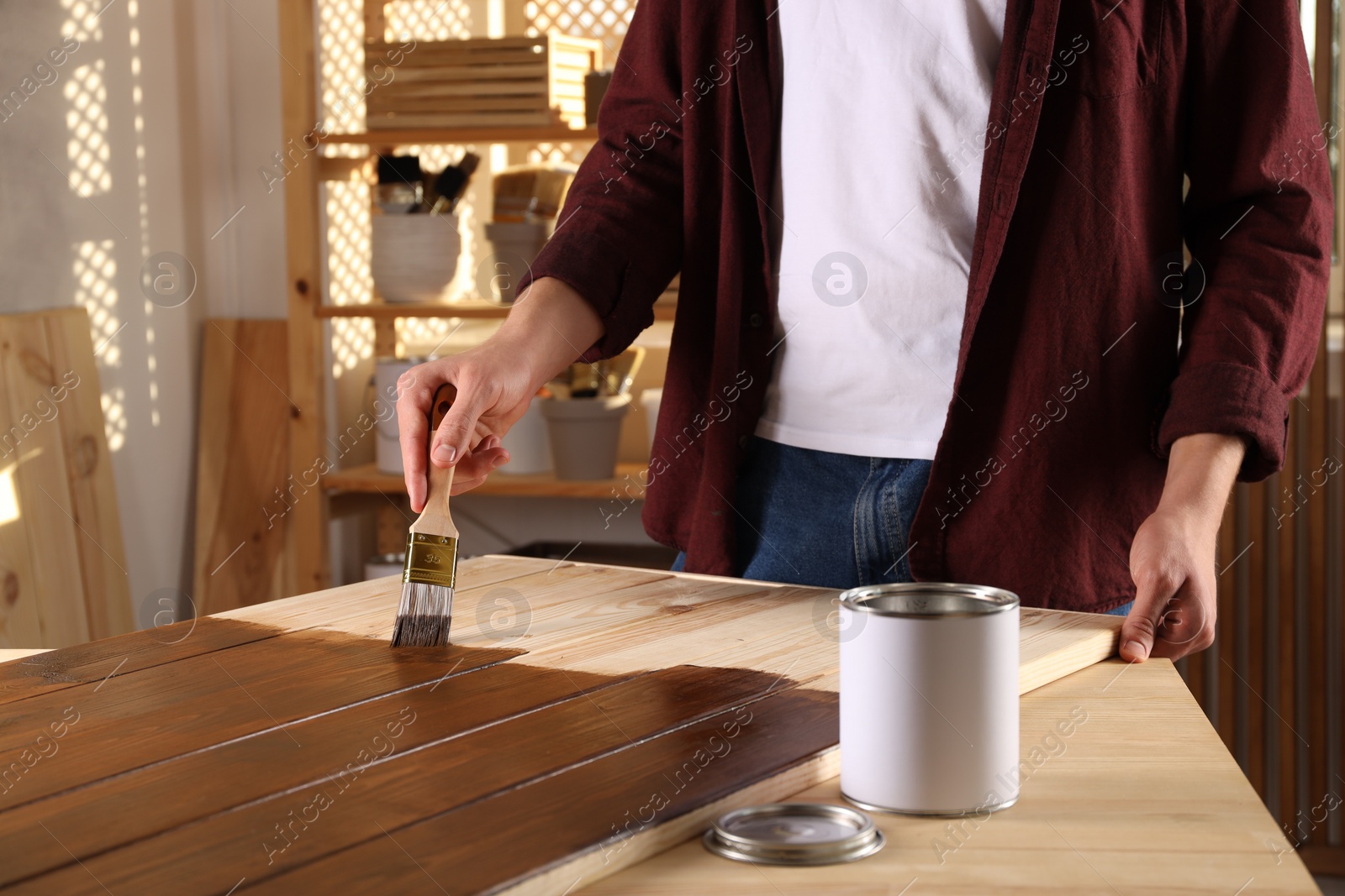 Photo of Man with brush applying wood stain onto wooden surface indoors, closeup