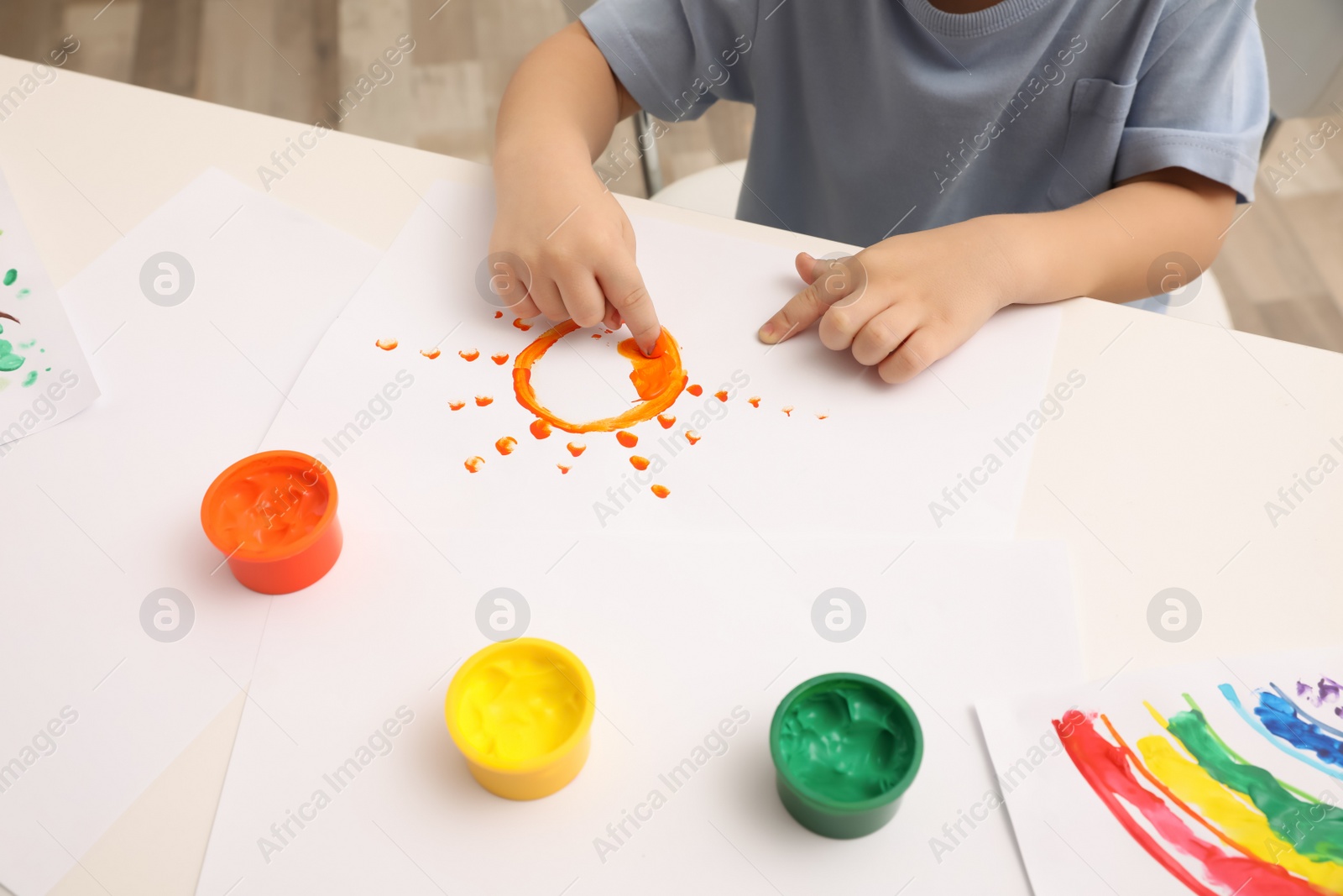 Photo of Little boy painting with finger at white table indoors, closeup