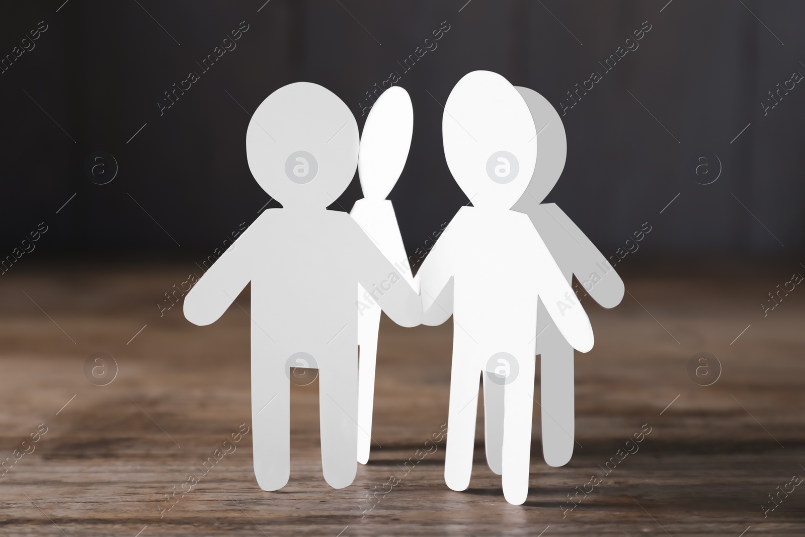 Photo of Teamwork concept. Paper figures of people holding hands on wooden table, closeup