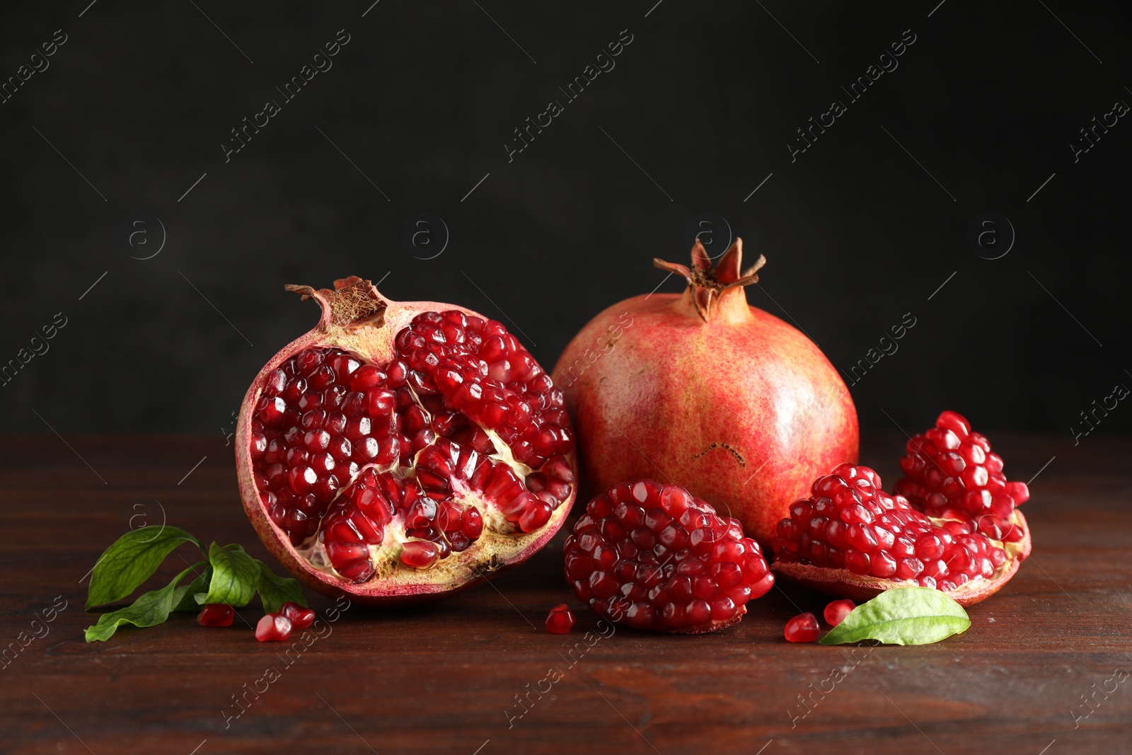 Photo of Fresh pomegranates and green leaves on wooden table