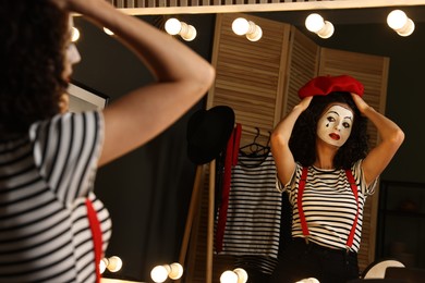 Young woman in mime costume putting beret near mirror indoors
