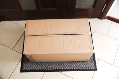 Photo of Cardboard box on rug near door, above view. Parcel delivery service