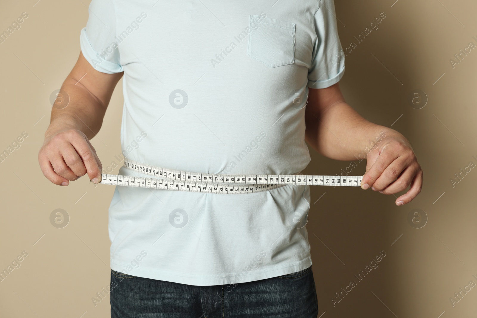 Photo of Man measuring waist with tape on beige background, closeup