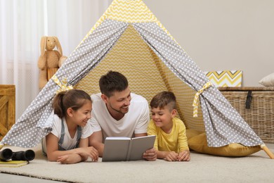 Father with children reading book in wigwam at home